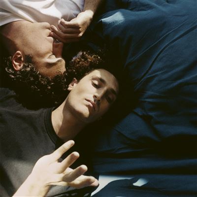 Visuel pour l'album Protégé-e de Terrenoire. En fond, un lit paré de draps bleus foncés. A gauche de l'image, les bustes du duo Terrenoire. Ils semblent encore à moitié endormis, leurs visages éclairés par un rayon de soleil venant presque se placer au centre de l'image.